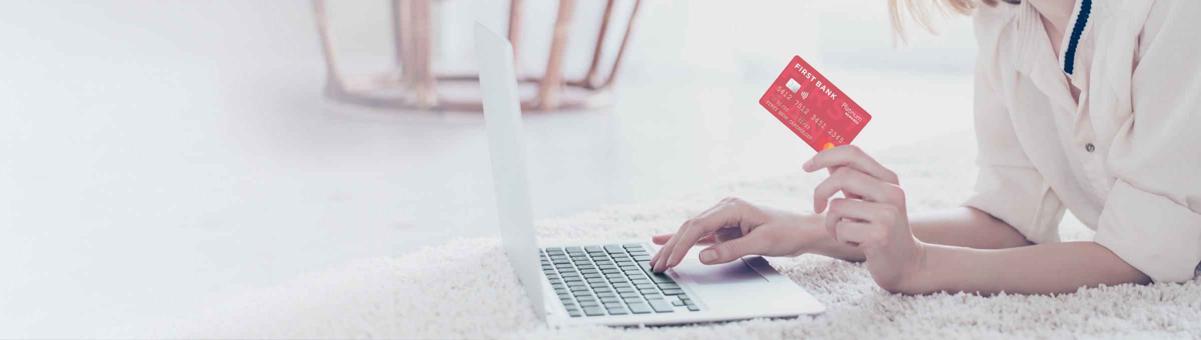 a woman holding her Crawfield Credit Union Platinum Rewards card while on the computer.